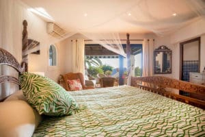 Photo of a bedroom with four poster bed and open doors leading to a tropical garden in the Costa del Sol by Jason Elliott